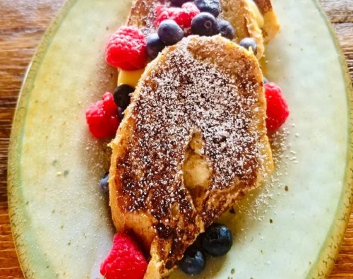 A plate of French toast topped with powdered sugar and fresh blueberries and raspberries.