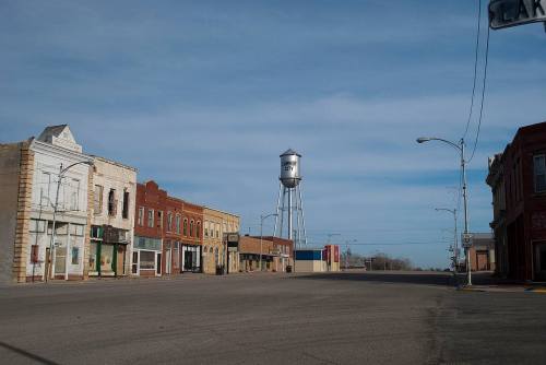 A quiet street in a small town featuring old brick buildings and a tall water tower against a cloudy sky.