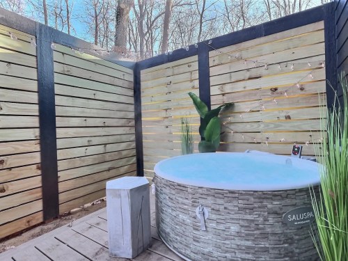 A cozy outdoor hot tub surrounded by wooden fencing and greenery, with soft lighting in a serene forest setting.