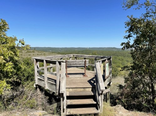 A wooden observation deck overlooks a lush green landscape under a clear blue sky.