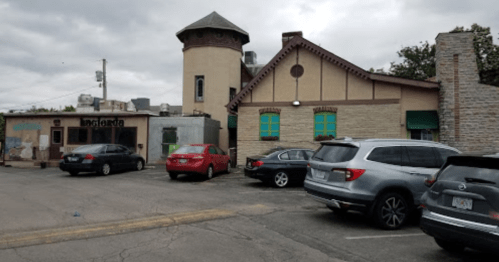 A parking lot with several cars in front of a unique building featuring a tower and colorful windows.