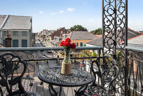 A balcony view featuring a table with a vase of red roses, overlooking a charming street with historic buildings.