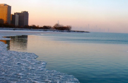 A serene winter scene of a frozen lake with city skyline in the background during sunset.
