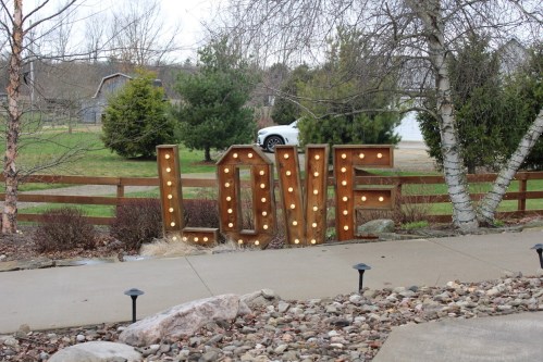 A large, illuminated "LOVE" sign stands in a landscaped area with trees and a gravel path.