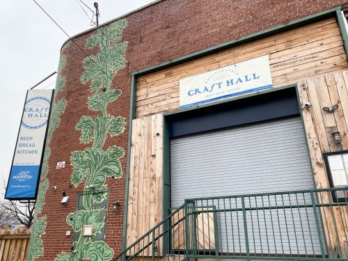 Exterior of Craft Hall featuring a brick wall with green vine artwork and a wooden entrance sign.