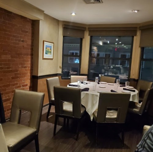 A cozy restaurant corner with a round table set for dining, surrounded by chairs and a brick wall.
