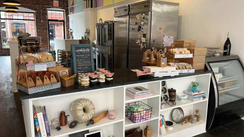 A cozy café interior featuring a display counter with baked goods, desserts, and a refrigerator in a bright space.