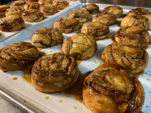 A tray of freshly baked cinnamon rolls drizzled with caramel, arranged neatly on parchment paper.