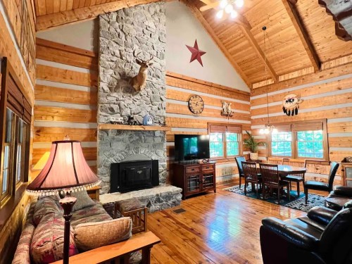 Cozy log cabin interior with a stone fireplace, wooden beams, and rustic decor, featuring a dining area and comfortable seating.