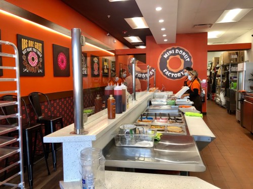 Interior of a donut shop with orange walls, a service counter, and staff preparing food. Decor includes donut-themed artwork.