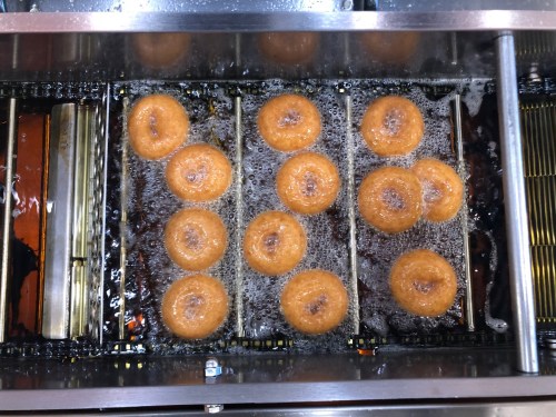 A top view of freshly fried donuts bubbling in hot oil on a fryer rack.