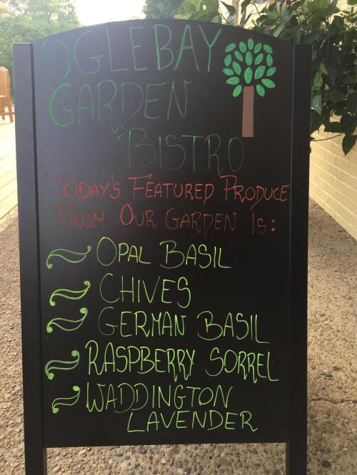 A chalkboard sign listing featured garden produce: opal basil, chives, German basil, raspberry sorrel, and Waddington lavender.