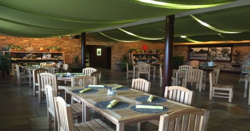A cozy restaurant interior with wooden tables, chairs, and green draped fabric overhead, featuring plants and decor.