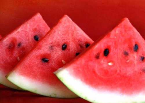 Three slices of juicy watermelon with black seeds, set against a vibrant red background.