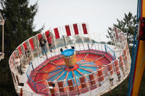 A colorful amusement park ride with a circular platform and people standing on it, surrounded by trees.