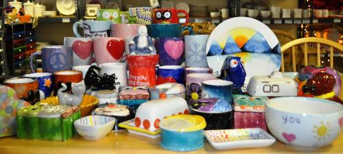 A colorful display of various hand-painted ceramic mugs, bowls, and decorative items arranged on a table.