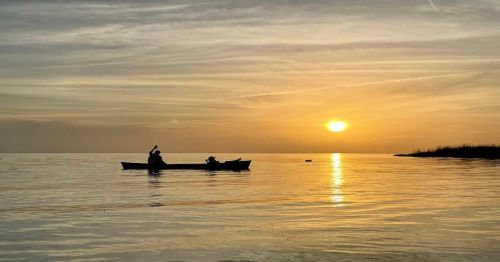 A serene sunset over calm waters, with a person kayaking silhouetted against the golden sky.
