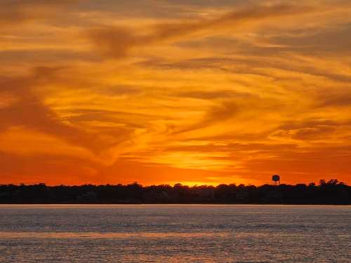 A vibrant sunset over a calm lake, with colorful clouds and a silhouette of a water tower in the distance.