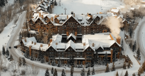 Aerial view of a large, snow-covered lodge surrounded by trees and a ski slope in a winter landscape.