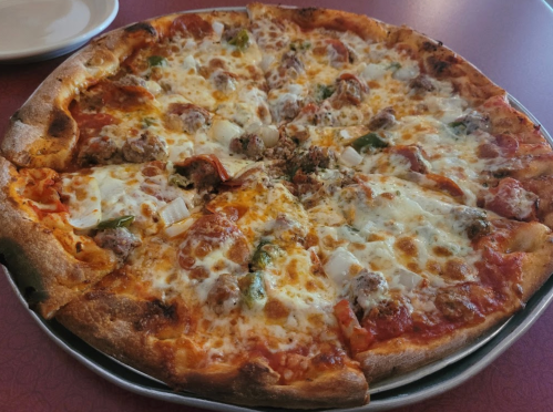 A large pizza topped with cheese, pepperoni, sausage, green peppers, and onions on a round tray.