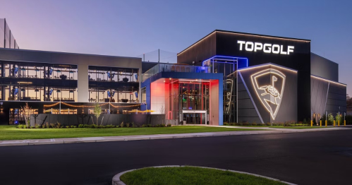 Exterior view of a Topgolf venue at dusk, featuring modern architecture and illuminated signage.