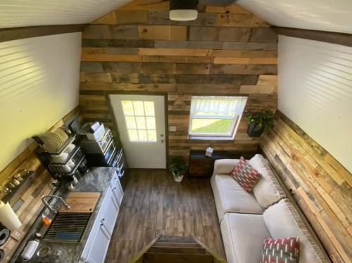 Cozy interior of a small cabin with wooden walls, a sofa, and a kitchen area, viewed from above.
