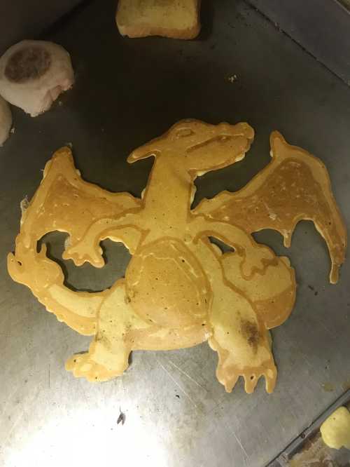 A pancake shaped like a dragon, featuring detailed wings and a rounded body, on a griddle.