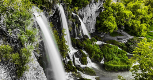 A serene waterfall cascading over rocks, surrounded by lush greenery and a peaceful pathway.