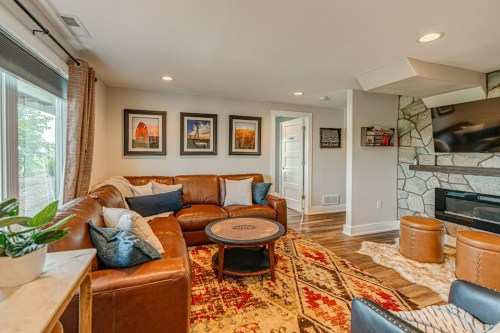 Cozy living room with a leather sofa, round coffee table, stone fireplace, and framed artwork on the walls.
