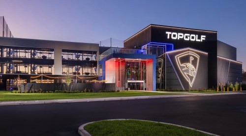 Exterior view of a Topgolf venue at dusk, featuring modern architecture and vibrant lighting.