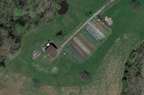 Aerial view of a rural property featuring a house, garden rows, and a small pond surrounded by greenery.