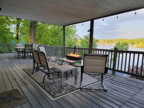 A cozy porch with seating and a fire pit overlooking a serene lake surrounded by greenery.