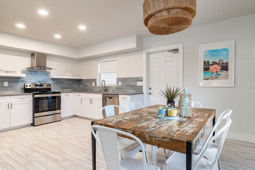 Bright kitchen with modern appliances, white cabinets, and a rustic dining table surrounded by white chairs.