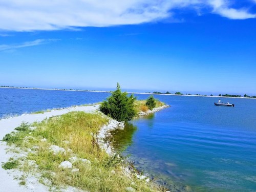 A serene landscape featuring a winding path between two bodies of water, with a small boat in the distance under a clear blue sky.