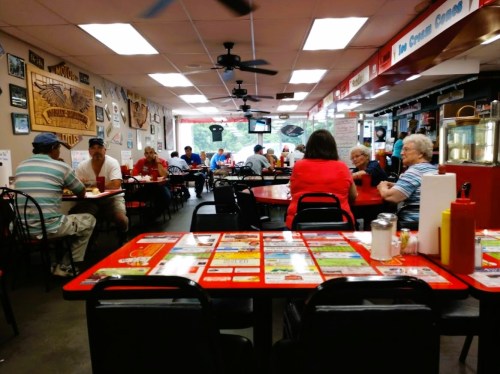 A busy diner with red tables, patrons enjoying meals, and a variety of decor on the walls.