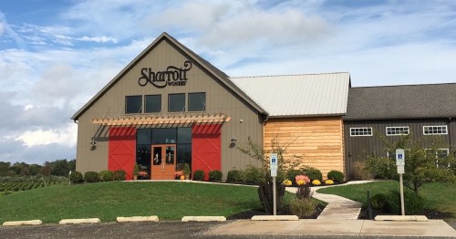 Exterior of Sharrot Winery featuring a modern building with red doors, landscaped grounds, and a cloudy sky.