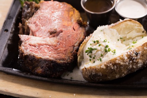 A plate featuring a juicy slice of roast beef with a baked potato topped with sour cream and chives.