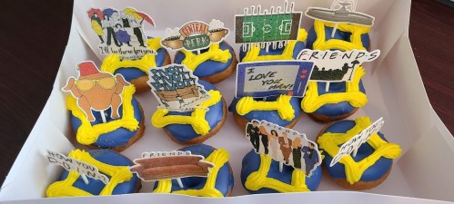 A box of blue donuts topped with colorful decorations and phrases from popular TV shows and themes.