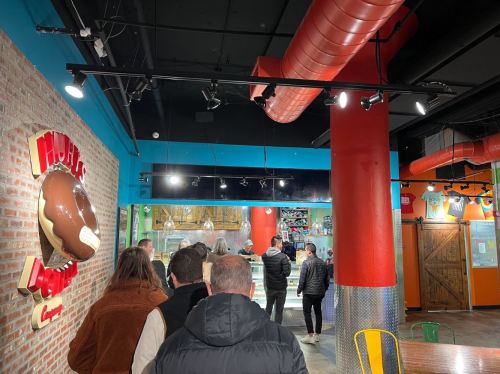 A line of people waiting in a colorful restaurant with exposed brick walls and bright decor.
