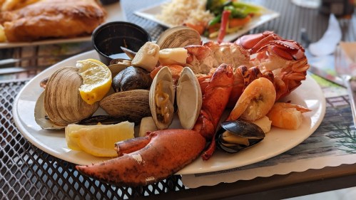 A seafood platter featuring lobster, clams, shrimp, and lemon wedges on a white plate.