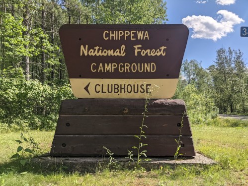 Sign for Chippewa National Forest Campground, directing to the clubhouse, surrounded by greenery and blue skies.