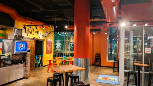 Colorful restaurant interior with bright walls, metal accents, and wooden tables. Pepsi machine visible in the corner.