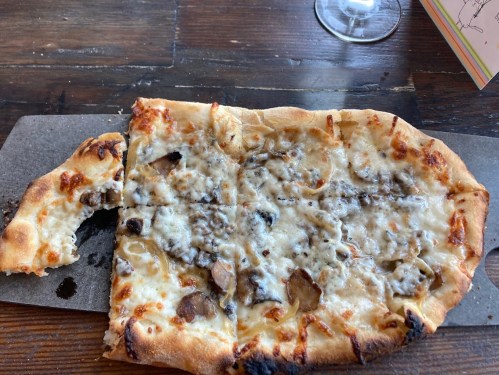A partially eaten flatbread pizza topped with melted cheese and mushrooms, served on a wooden board.