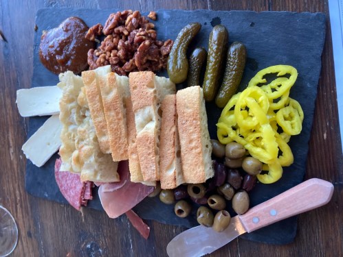 A charcuterie board featuring cheeses, meats, pickles, olives, nuts, and crackers on a slate platter.