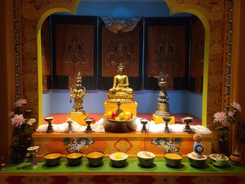 A colorful altar featuring a seated Buddha statue, surrounded by offerings and decorative elements.
