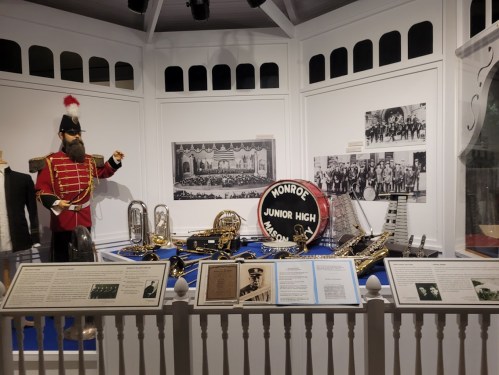 Display of musical instruments and uniforms from Monroe Junior High, featuring a large drum and historical photos.