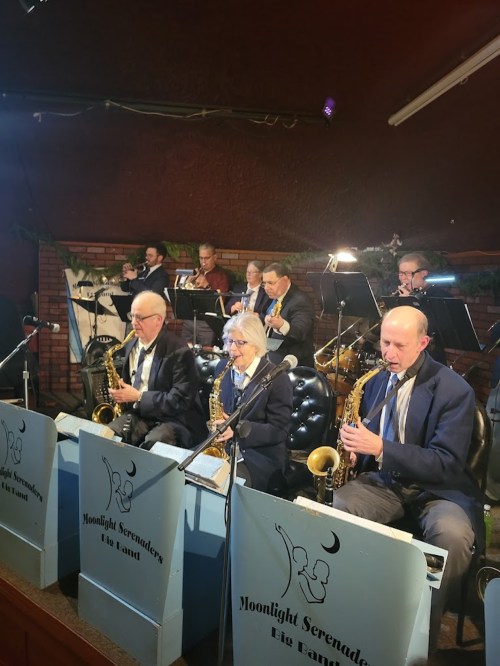A jazz band performs on stage, featuring musicians with saxophones and a full ensemble in a cozy venue.