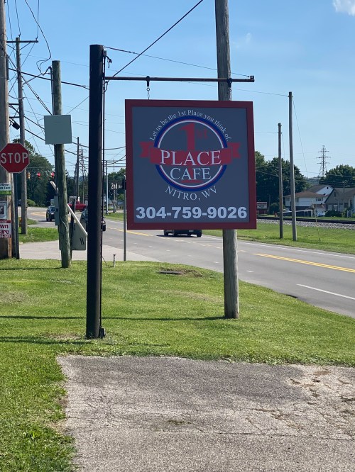 Sign for "1st Place Cafe" in Nitro, WV, with contact number 304-759-9026. Green grass and road visible in background.