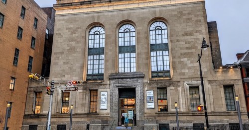 Historic building with large windows and stone facade, featuring a sign for "Science and Industry" at dusk.