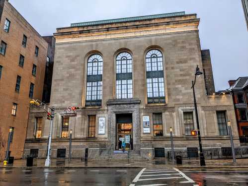 Historic building with large windows and decorative stonework, located on a rainy street corner.